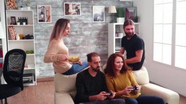 Uzun saçlı sakallı adam oturma odasında cips yiyor.