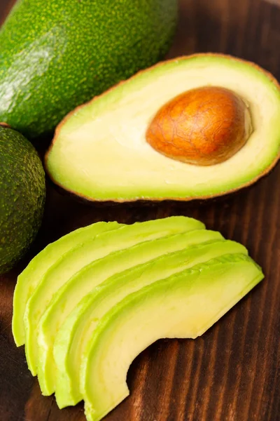 Rebanadas de aguacate junto a una cortada en una tabla de madera — Foto de Stock