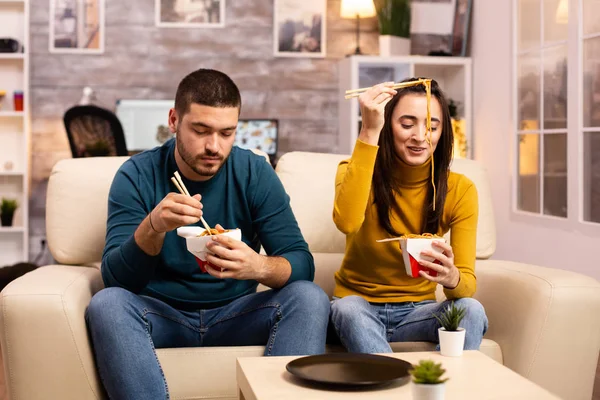 Na moderna e acolhedora sala de estar casal está desfrutando de macarrão takeaway enquanto assiste TV — Fotografia de Stock