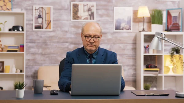 Bello vecchio prendere un sorso di caffè mentre si lavora sul computer portatile — Foto Stock