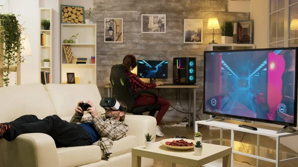 Man som ligger på soffan och spelar TV-spel med vr headset — Stockfoto