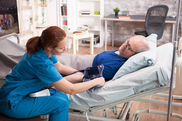 Female nurse doing a blood pressure check up on old man — ストック写真