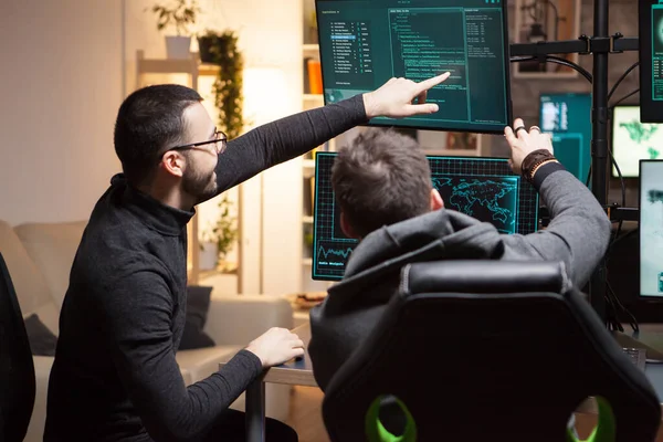 Achteraanzicht van hackers die op computerschermen wijzen — Stockfoto