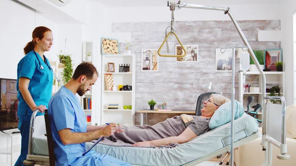 Команда медсестер-мужчин и женщин проверяет старушку, лежащую на больничной койке — стоковое фото