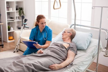 Female caregiver with cliboard talking with sick woman