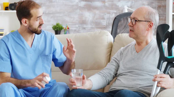 Чоловіча медсестра дає таблетки пенсіонеру в будинку престарілих — стокове фото
