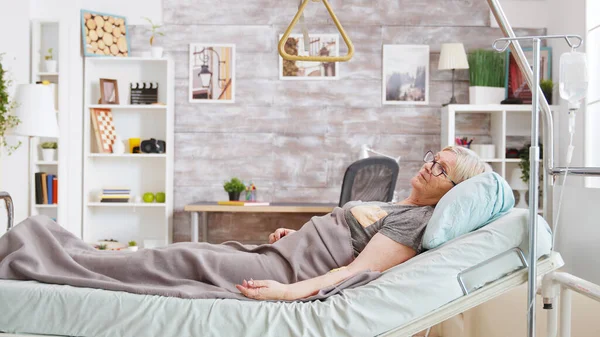 老人ホームで居心地の良い明るい部屋で病院のベッドに横たわっている障害者の女性 — ストック写真