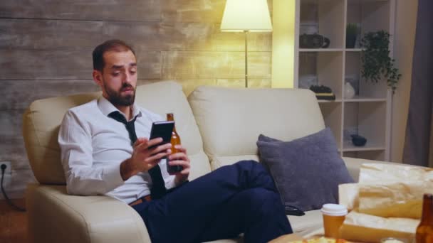 Втомився бізнесмен сидить на дивані, прокручуючи свій телефон — стокове відео