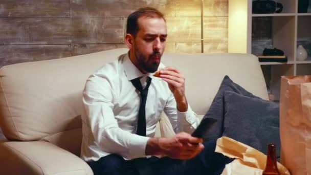 Empresario con corbata comiendo una hamburguesa mientras ve la televisión — Vídeos de Stock