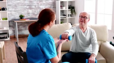 Caucasian caregiver in nursing home helping an old man to recover muscle strength
