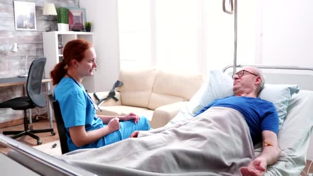 Medico donna parlando vecchio sdraiato a letto in una casa di cura — Video Stock