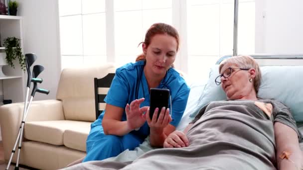 Female nurse helping old woman to use smartphone — Stockvideo