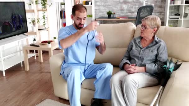 Médico en casa de ancianos escuchando latidos del corazón de anciana — Vídeos de Stock