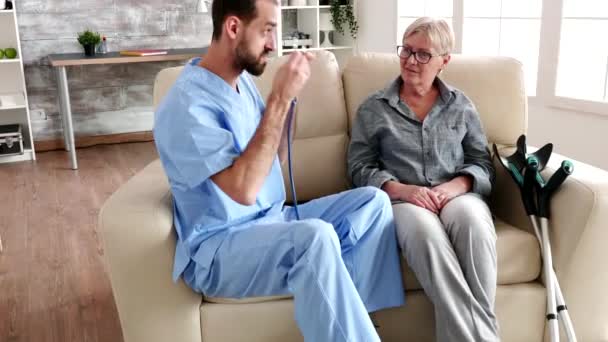 Enfermera masculina escuchando latidos del corazón de una anciana con un estetoscopio — Vídeos de Stock