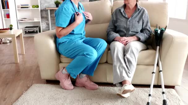 Female asistant in retirement home listening old woman heartbeat — Wideo stockowe