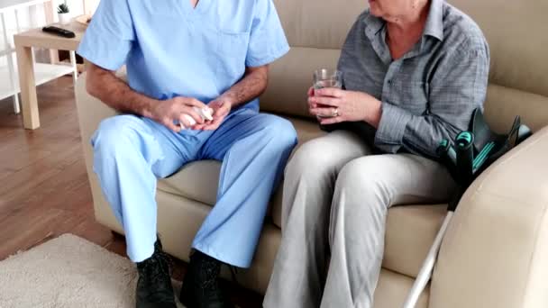 Enfermera masculina en sofá con anciana jubilada que le da tratamiento médico en casa de retiro — Vídeo de stock