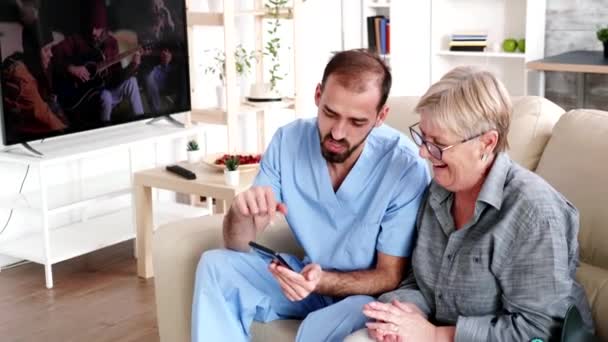 Enfermera en casa de retiro ayudando a una anciana a usar su teléfono — Vídeo de stock