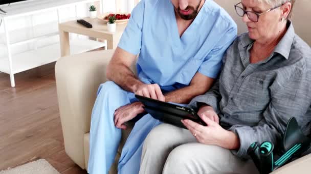 Enfermera masculina enseñando anciana anciana cómo utilizar su tableta PC — Vídeos de Stock