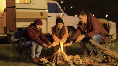 Kamp ateşi etrafında kamp sandalyelerinde oturan yakın bir arkadaş.