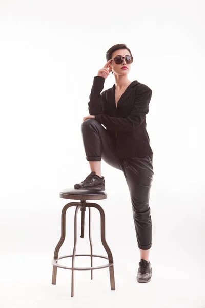 Молодая модель в модной и повседневной одежде позирует в студии, используя стул на белом фоне — стоковое фото