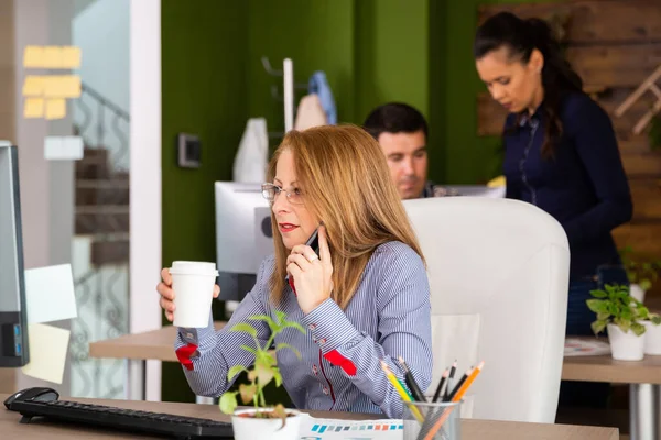Сосредоточенная деловая женщина, заглядывающая в монитор компьютера, пока разговаривает по телефону — стоковое фото