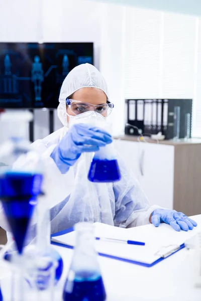 Onderzoeker heeft zijn ogen gefixeerd op een container met een blauwe vloeistof — Stockfoto