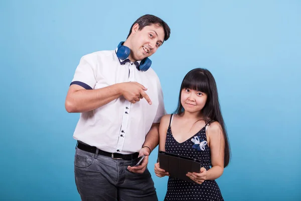 Asiático namorada segurando tablet e namorado caucasiano apontando para ele em estúdio — Fotografia de Stock