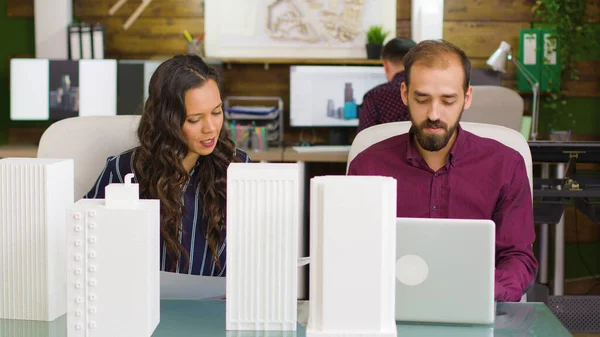 Designer trabalhando em um laptop e arquiteto olhando para plantas — Fotografia de Stock