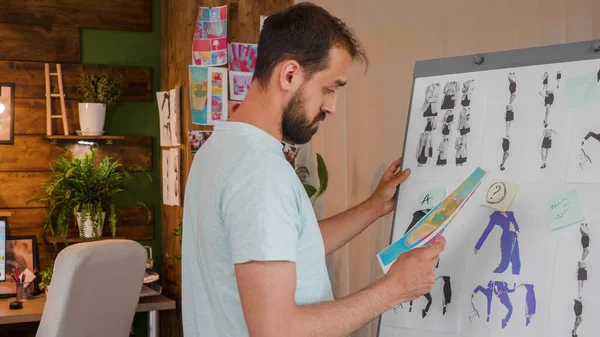 The designer boy looks at a printed picture that he holds in his hand near a whiteboard — Stockfoto