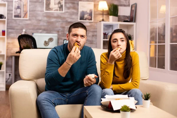 Jovem casal comer frango frito na frente da TV — Fotografia de Stock