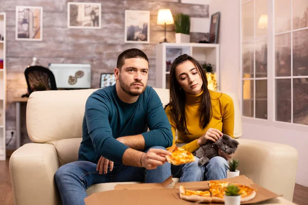 Прекрасная молодая пара ест пиццу во время просмотра телевизора — стоковое фото