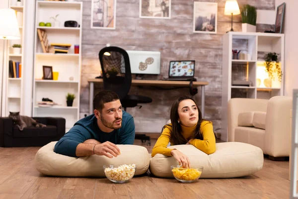 Casal sentado no chão e assistindo TV em sua sala de estar — Fotografia de Stock