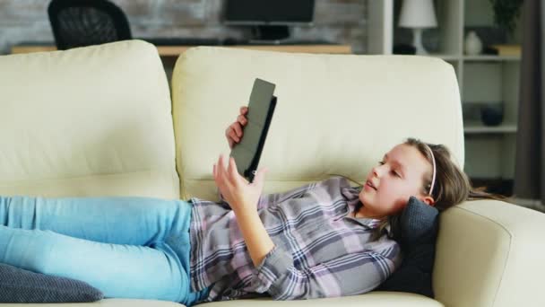 Klein meisje liggend op de bank met behulp van haar tablet — Stockvideo