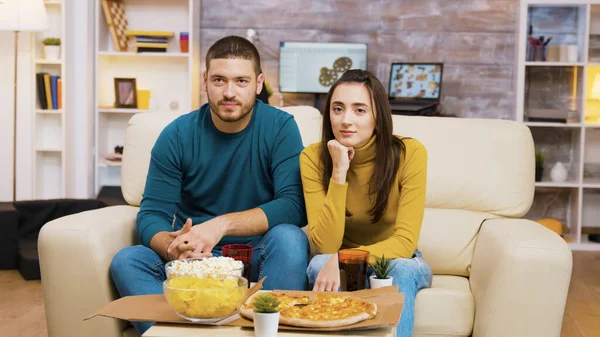 Pár sedí na gauči směje se při sledování televize a jíst pizzu — Stock fotografie