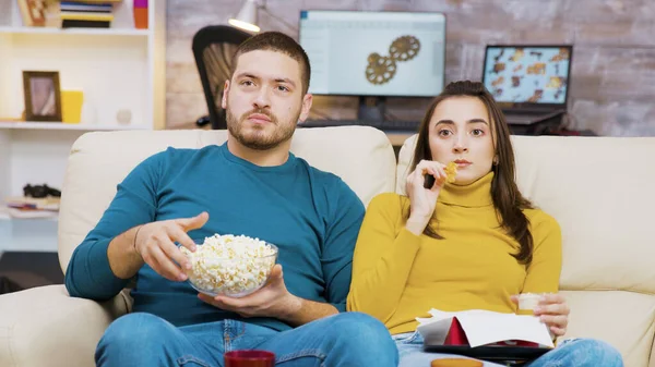 Vyděšený pár sleduje televizi jíst pizzu a popcorn sedí na gauči — Stock fotografie