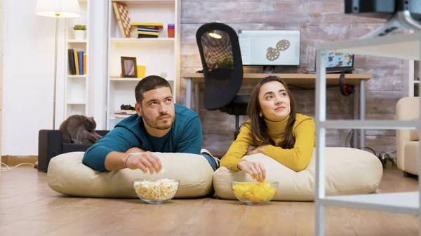 Веселая пара смотрит телевизор, сидя на подушках — стоковое фото