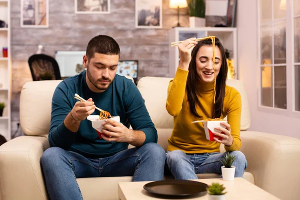 Na moderna e acolhedora sala de estar casal está desfrutando de macarrão takeaway enquanto assiste TV — Fotografia de Stock