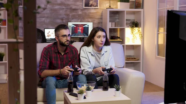 Веселая молодая пара, сидящая на диване и играющая в видеоигры — стоковое фото