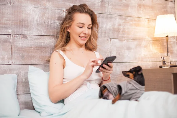 Красива жінка в піжамі посміхається, використовуючи свій телефон — стокове фото