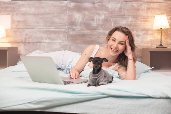 Молода жінка сміється під час використання свого ноутбука в ліжку — стокове фото