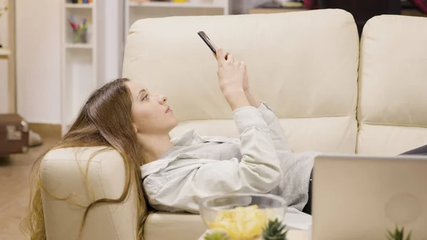 Chica bonita relajándose en el sofá usando su teléfono inteligente — Foto de Stock