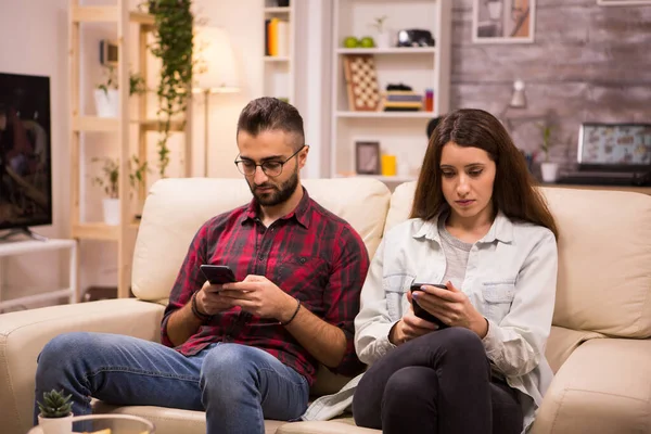 Petit ami et petite amie en utilisant leurs téléphones tout en étant assis ensemble sur le canapé — Photo