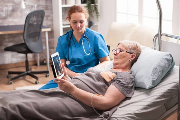 Oude vrouw in verpleeghuis zittend in bed met behulp van tablet computer — Stockfoto