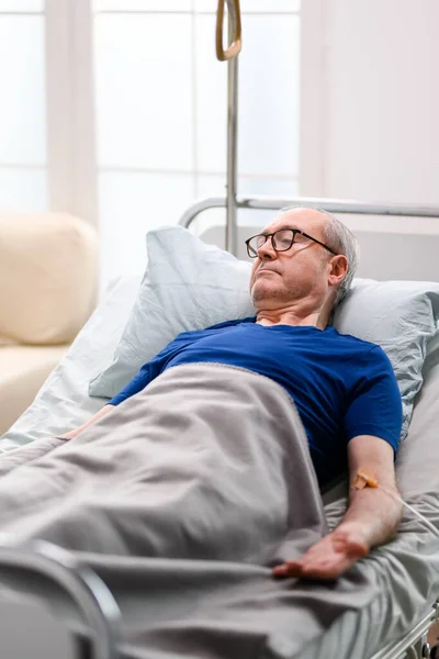 Gepensioneerde oude man in verpleeghuis liggend op bed — Stockfoto