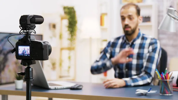 Vlogger sentado en el escritorio en la sala de estar hablando y mirando a la cámara — Foto de Stock