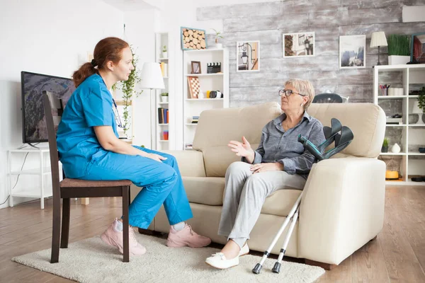 Enfermera en una silla en un hogar de ancianos hablando con una mujer de edad avanzada — Foto de Stock