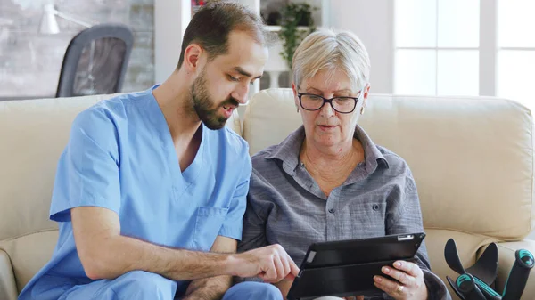 Assistente maschile insegnamento anziana anziana anziana anziana in pensione come utilizzare il suo computer tablet — Foto Stock