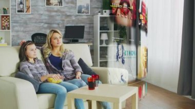 Kanepede oturan aile, önlerindeki akıllı televizyonun sanal bir yansımasını izliyor.