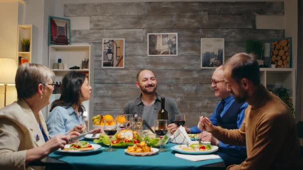 Молодой человек рассказывает анекдот на воскресном семейном ужине — стоковое видео