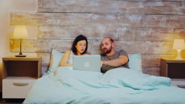 Молодая пара в пижаме делает покупки на ноутбуке — стоковое видео
